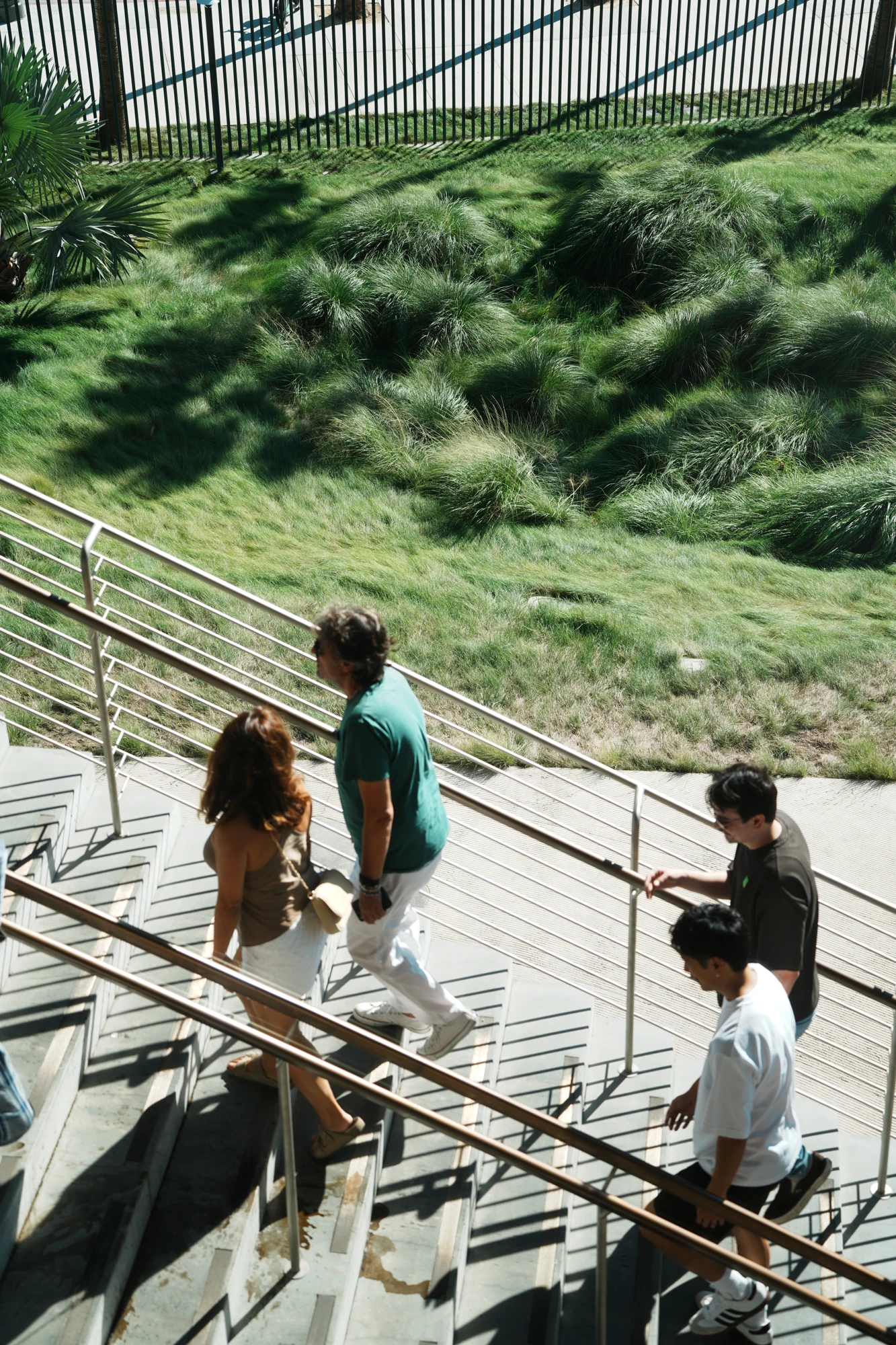 People climb an outdoor staircase beside a grassy slope.