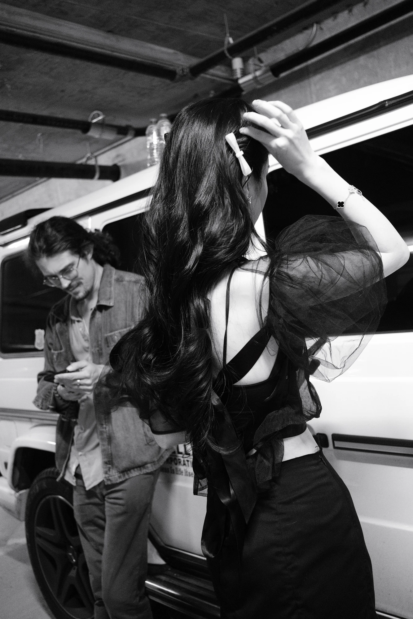 A woman lifts her hair beside a man in a black-and-white candid scene.