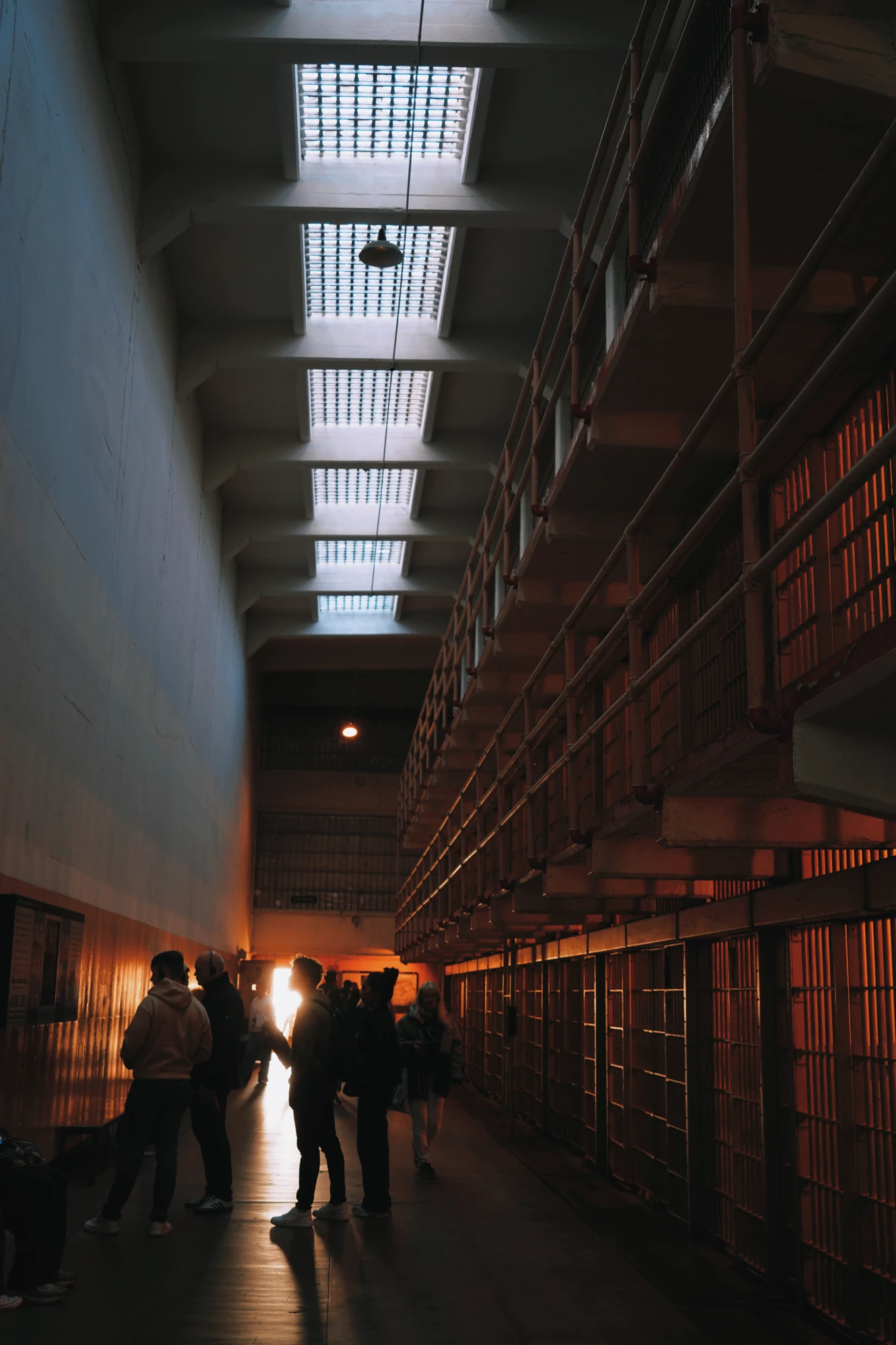 Visitors walk along a long cellhouse corridor toward a bright doorway.