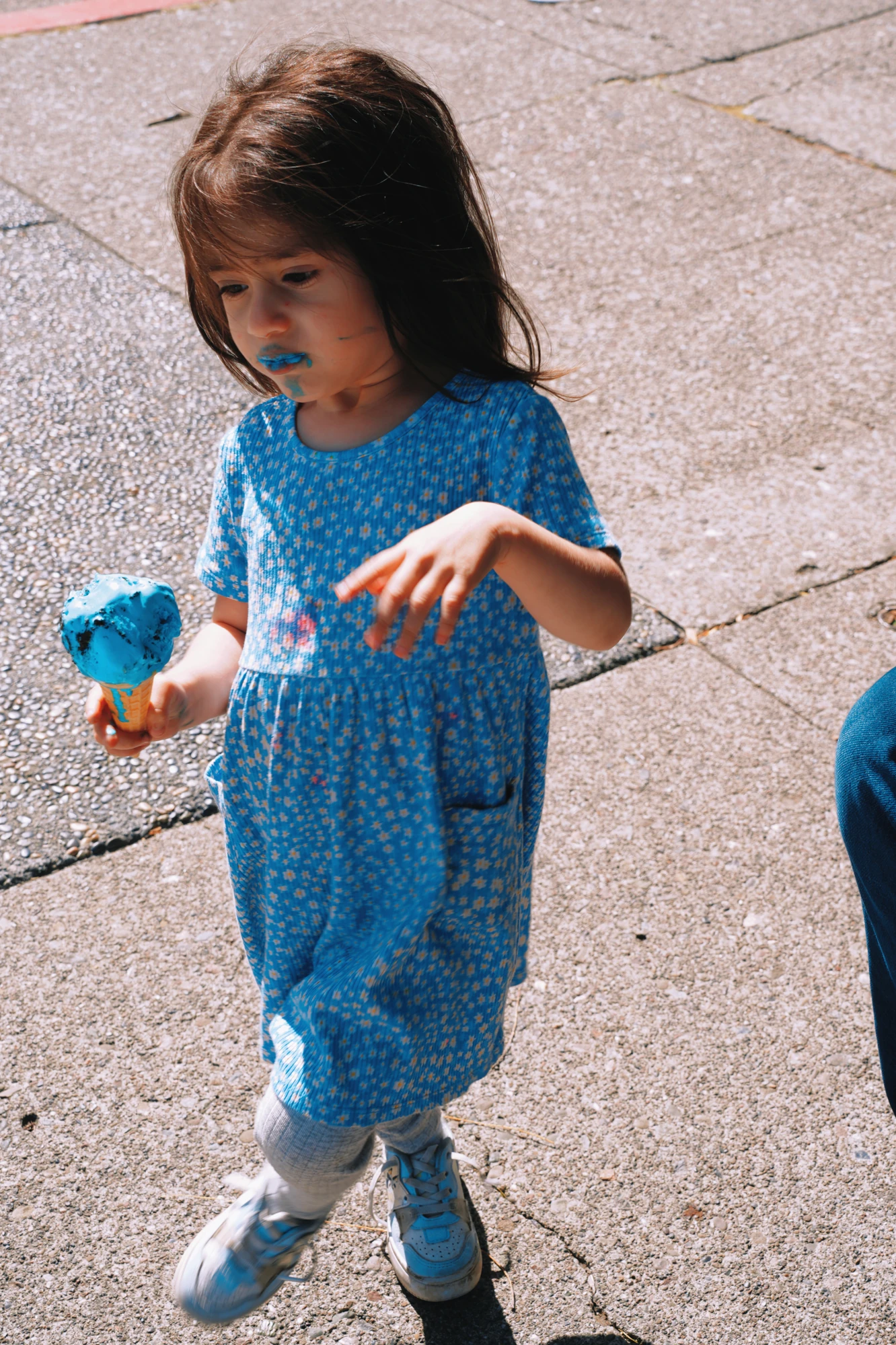 A little girl in a blue dress holds a blue ice cream.