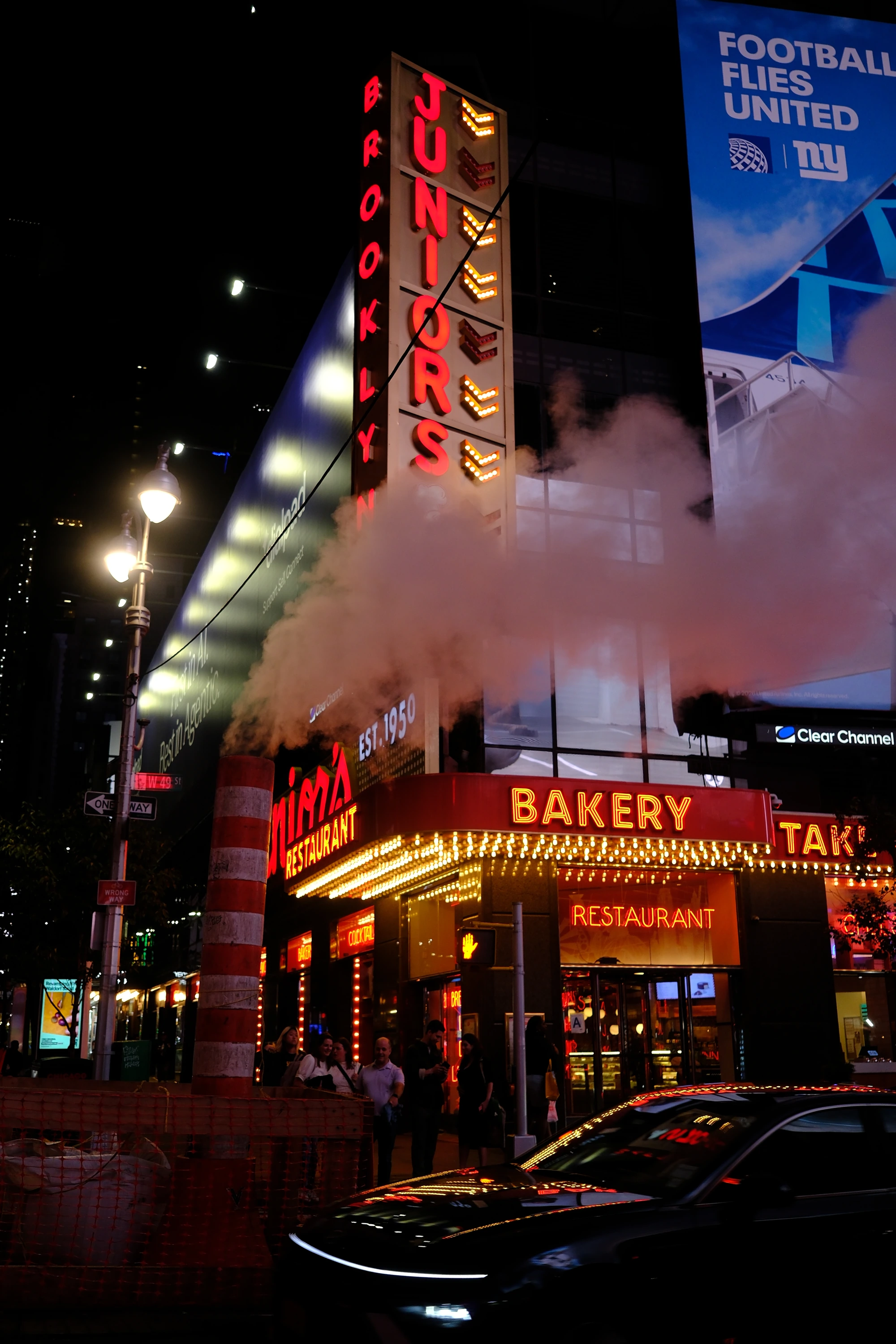 Steam rises past neon signs on a New York street at night.