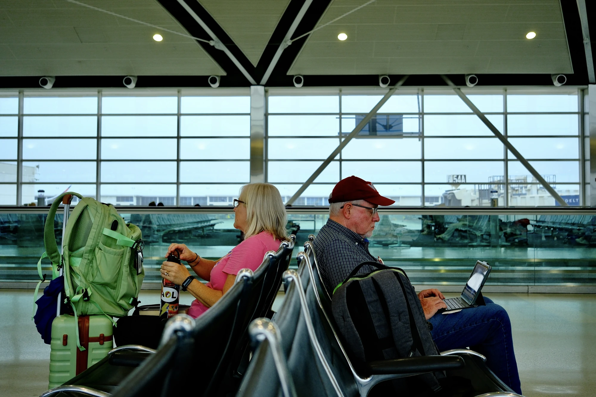 Travelers sit in rows beneath the angular roof of an airport terminal.