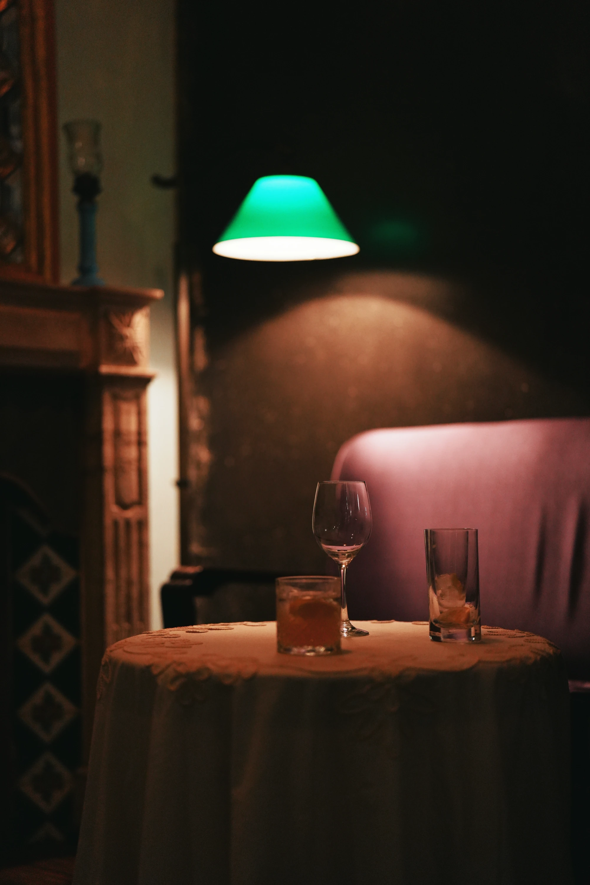 A green lamp lights a quiet bar table with two glasses.
