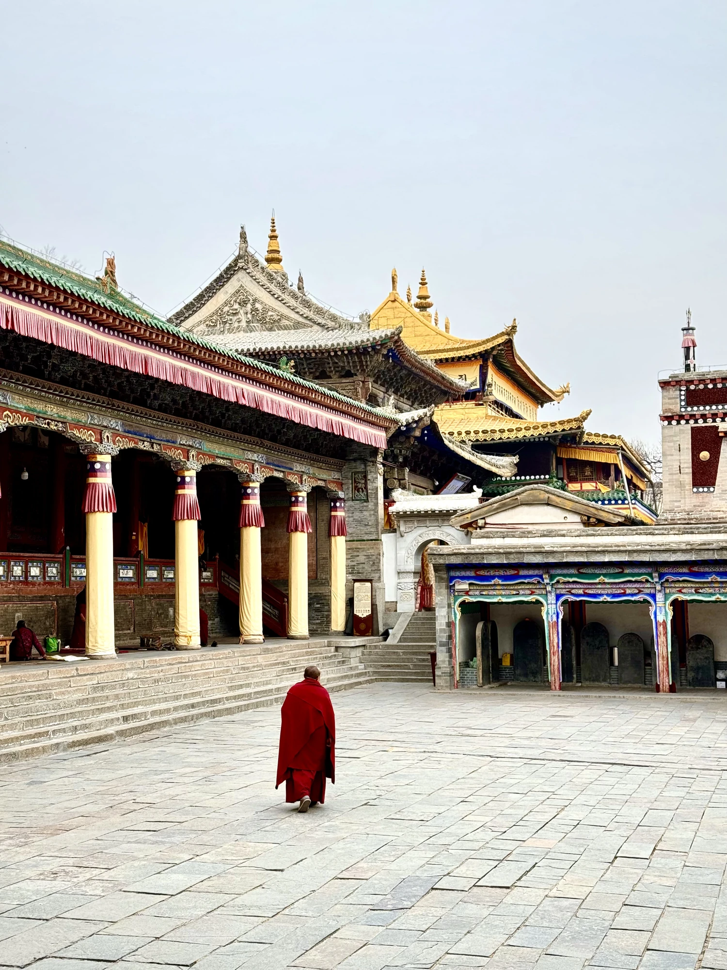 A red-robed figure crosses a paved temple courtyard.