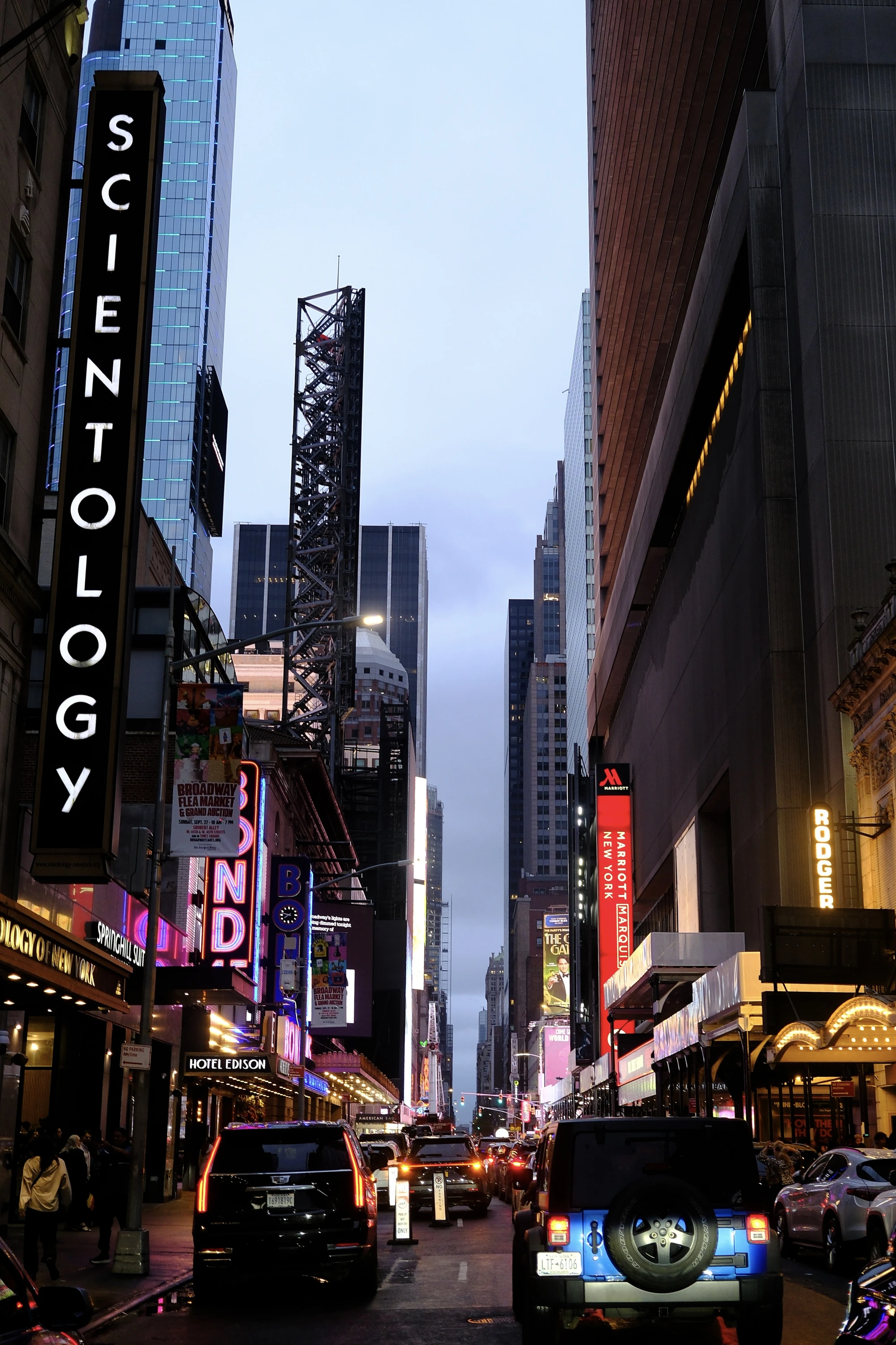 A Scientology sign and traffic in a narrow Midtown canyon at dusk.