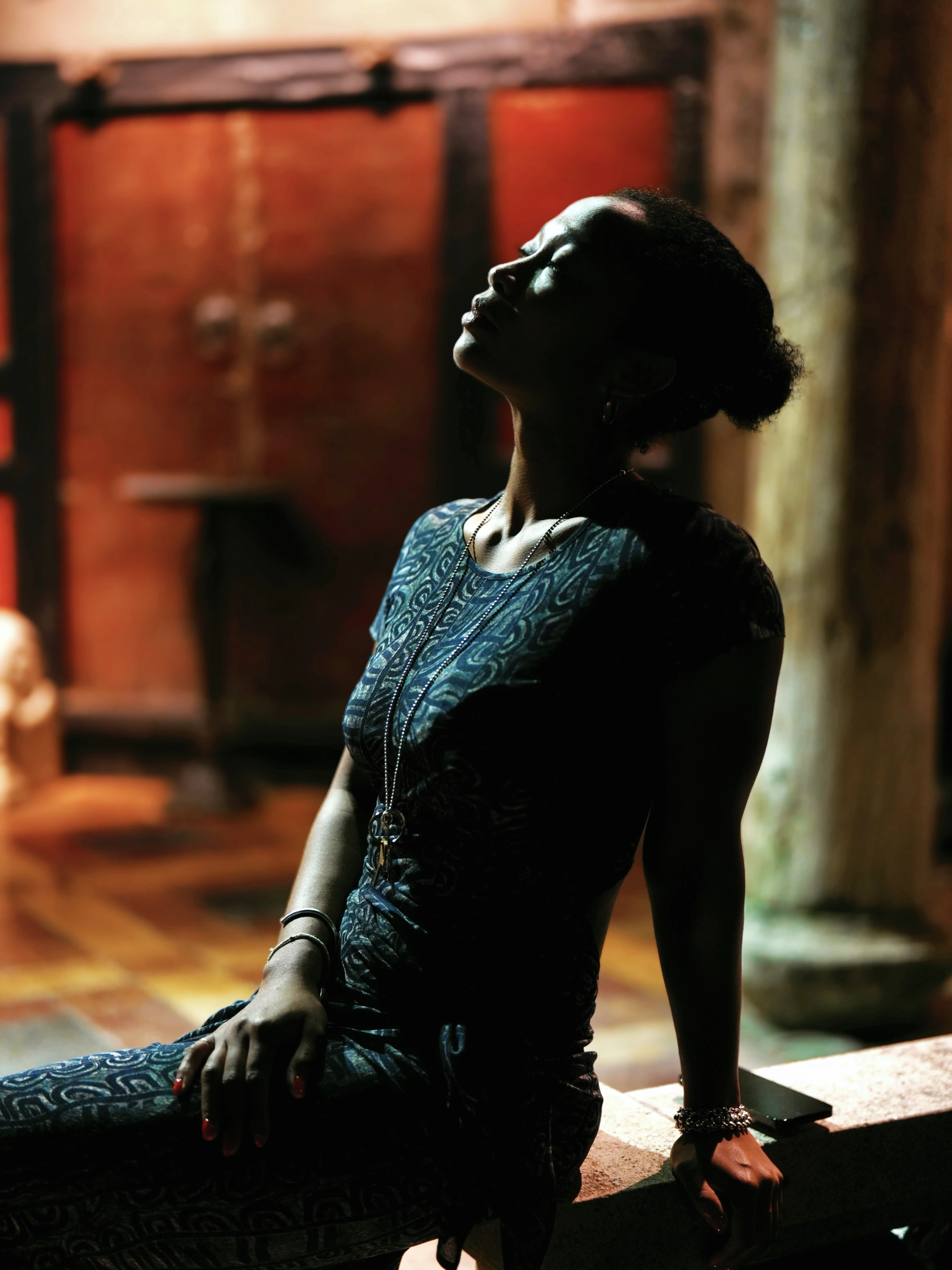 A woman in a patterned dress lifts her face toward warm light.