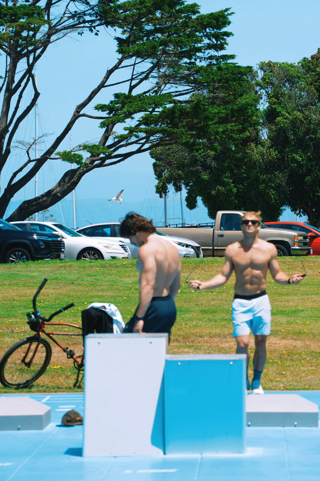 Two men exercise in a waterfront park beside a bicycle.